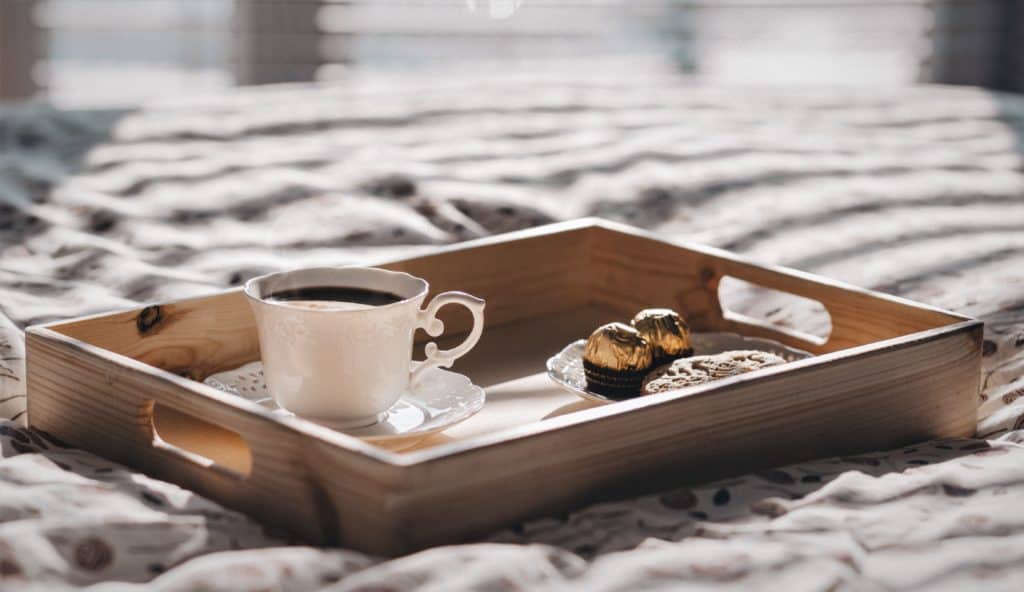 cup of coffee with chocolates on a tray on a bedspread