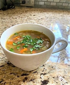 White soup mug containing chicken soup sprinkled with parsley