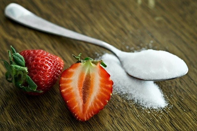 Cut strawberry next to spoonful of sugar