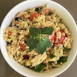 white bowl of couscous salad with fresh oregano leaves
