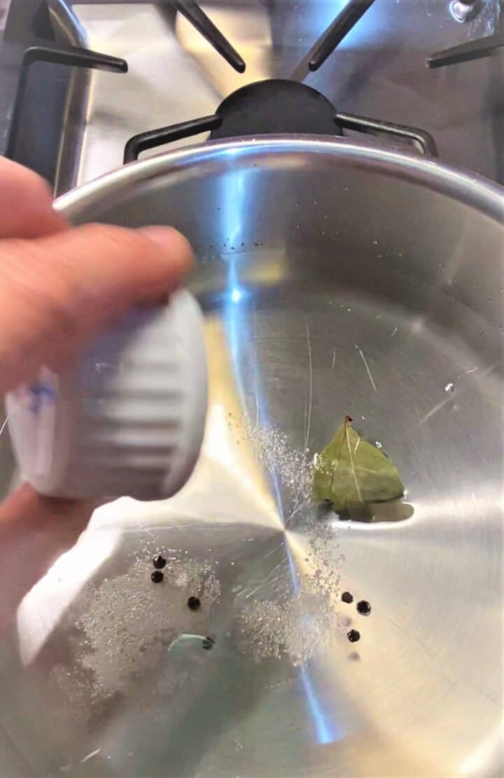 Pouring salt and peppercorns into water-filled skillet containing a bay leaf