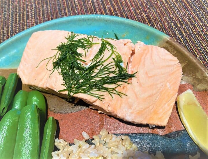 Teal and brown pottery plate with pink salmon fillet topped with dill, green snap peas, lemon wedge, and dab of fluffy rice