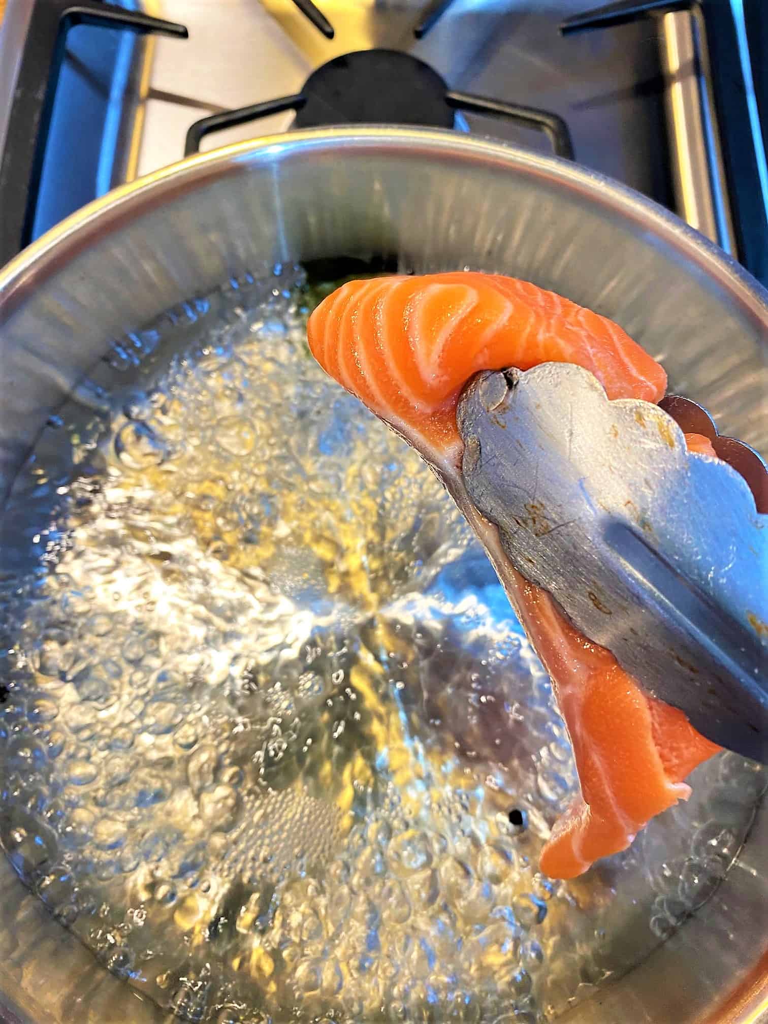 Using tongs to put a salmon fillet in a skillet of boiling water