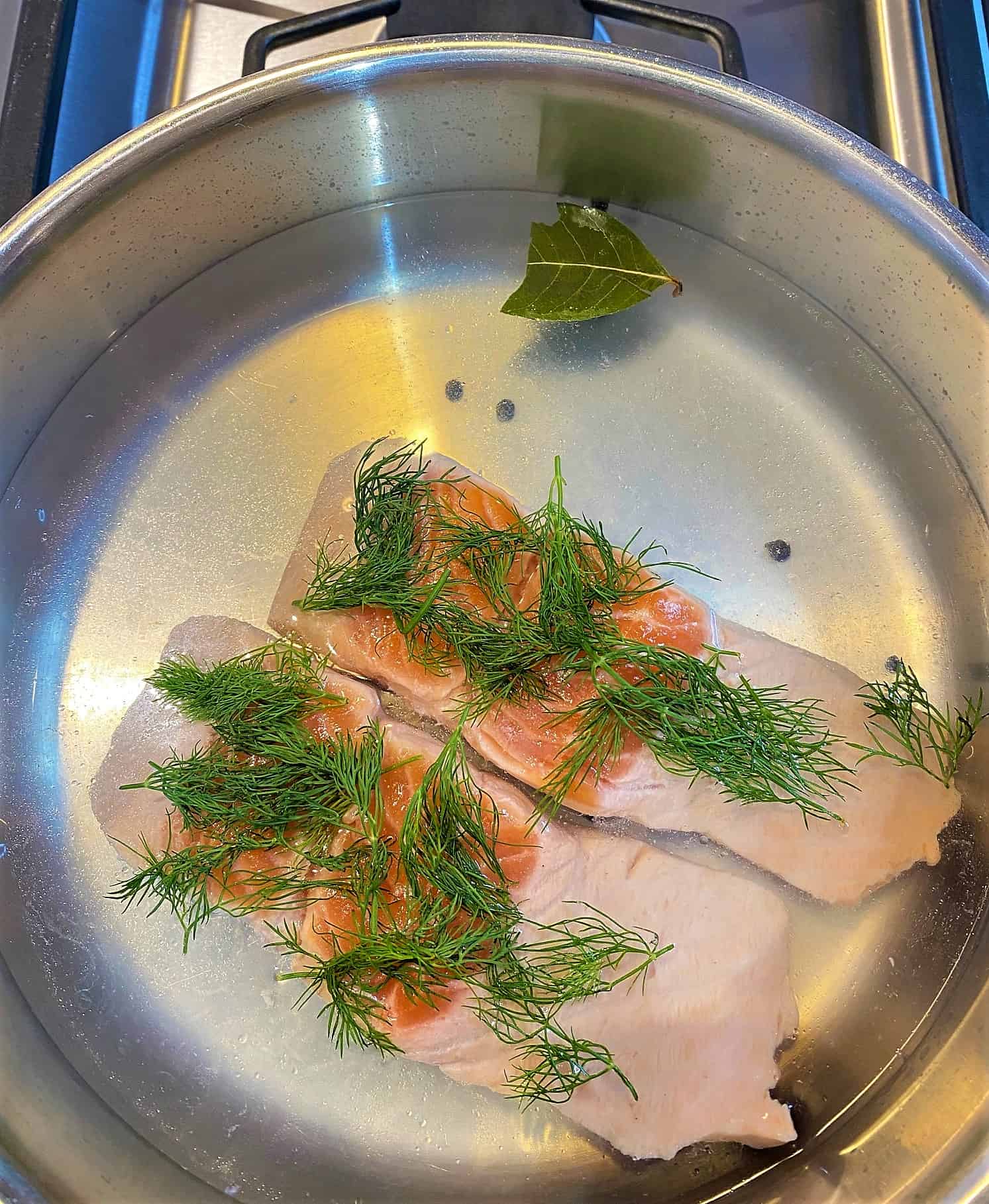Salmon fillets in a skillet of water topped with dill