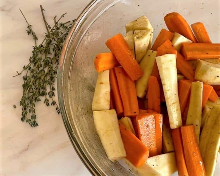 Raw carrot and parsnip logs in clear bowl with fresh thyme alongside.