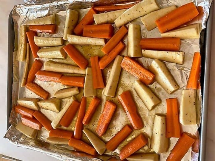 Carrot and parsnip logs with seasonings on foil in roasting pan.