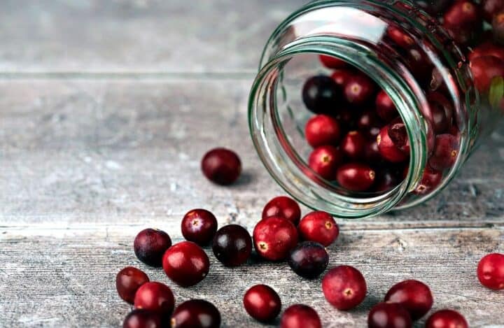 Jar of fresh cranberries spilled on gray surface.