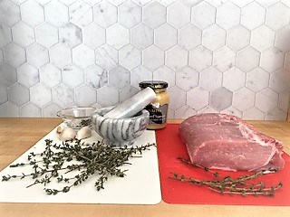 raw pork roast on red cutting board with fresh thyme and mustard