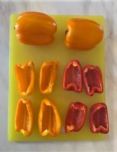 Whole yellow bell peppers with red and yellow quartered peppers on cutting board