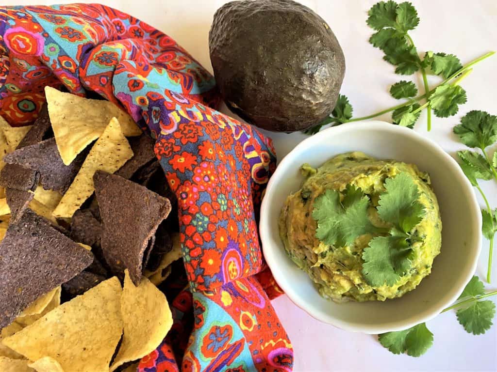 macamole (guacamole) with basket of blue and white tortilla chips, fresh cilantro and avocado