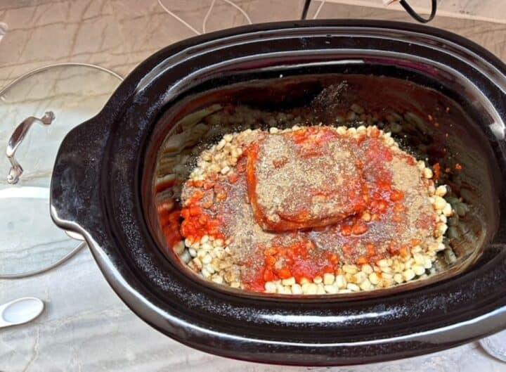 Black slow cooker liner with hominy corn and pork topped with red chile.
