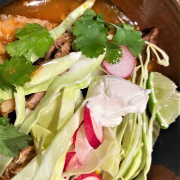 Pork posole topped with shredded cabbage, sliced radishes, cilantro, and dollop of sour cream