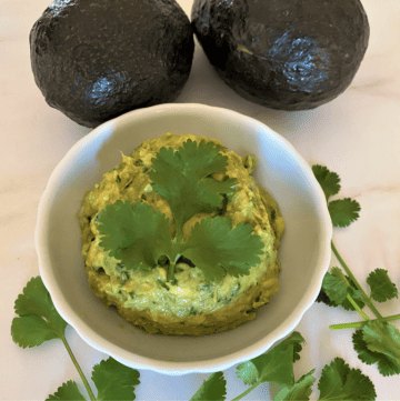 bowl of macamole (guacamole) with cilantro and 2 avocados