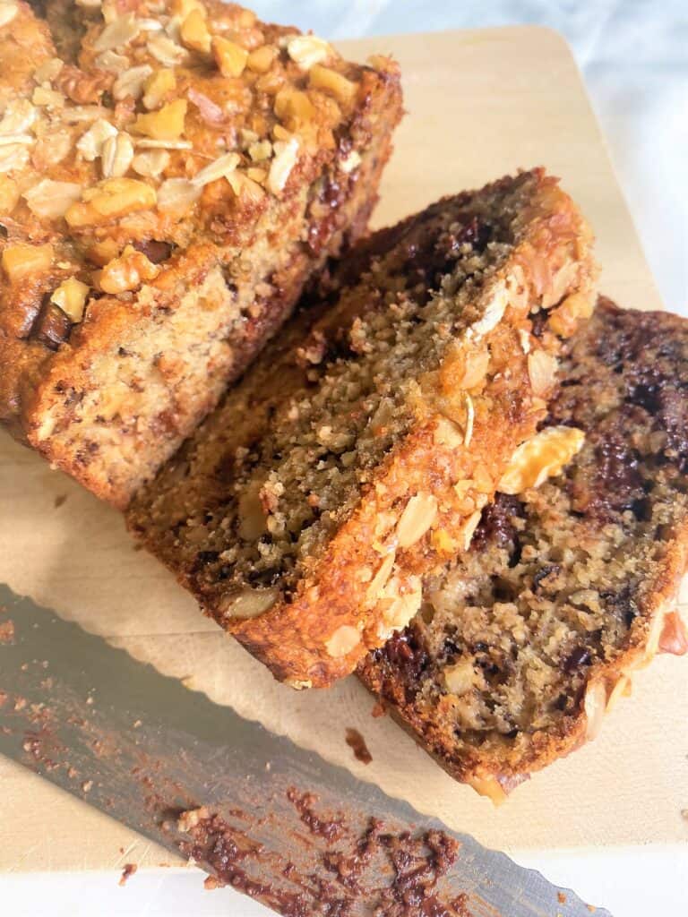 banana bread with oat flour and chocolate chunks sliced on wooden cutting board