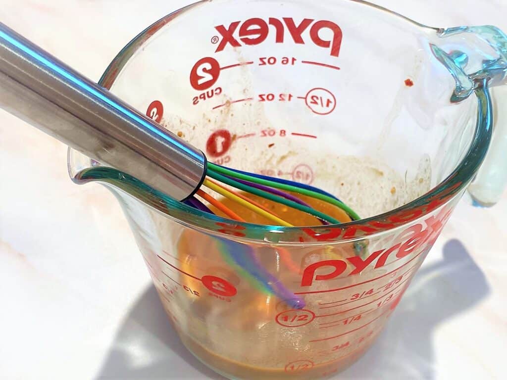Measuring cup with whisk and Asian marinade for chicken thighs
