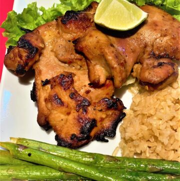 grilled boneless chicken thighs with a lime wedge, brown rice and asparagus