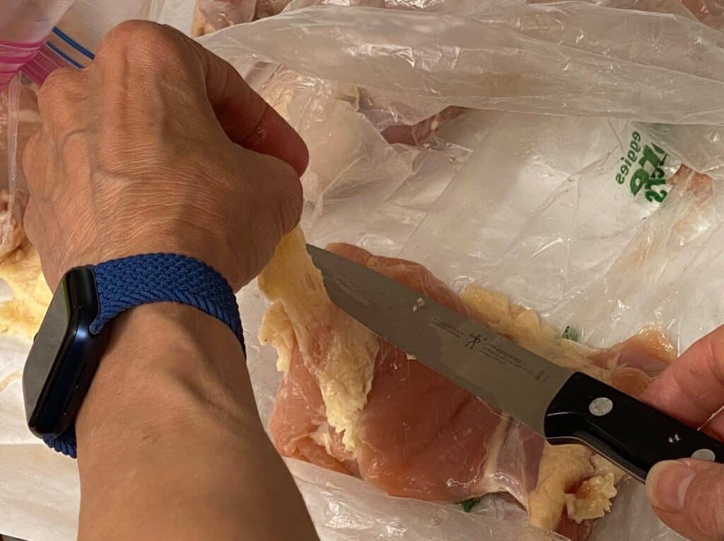 Removing some of the fat from boneless, skinless chicken thighs with a sharp knife