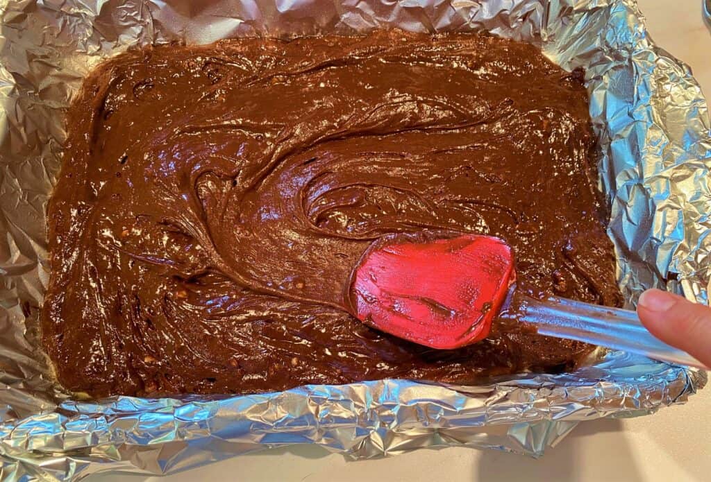 Scraping carb-conscious erythritol brownie batter into pan with red spatula