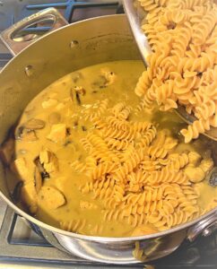 Pouring chickpea pasta into Creamy Coconut Chicken Curry