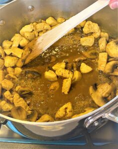 Adding broth to the skillet of Creamy Coconut Chicken Curry