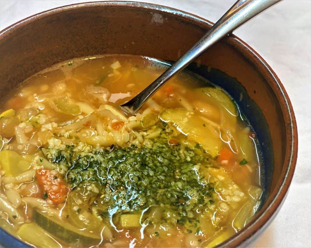 A bowl of Minestrone di Verdure, an Italian soup topped with pesto