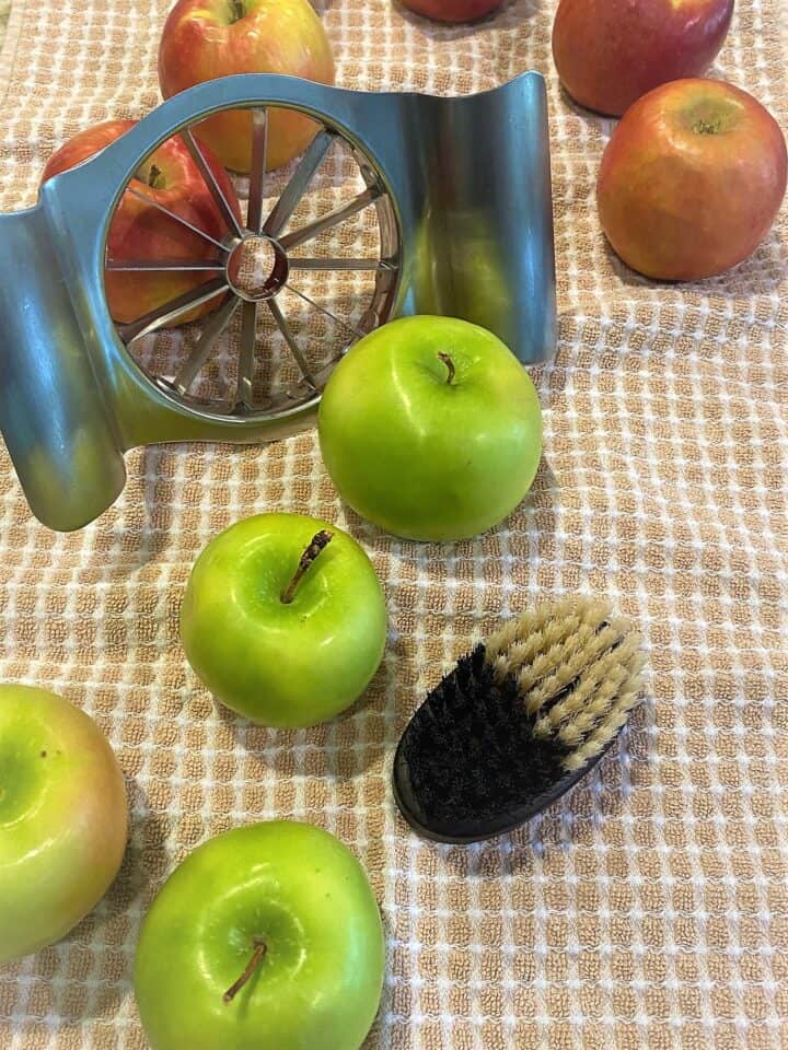 Green and red apples with a corer and scrub brush on ran and white tea towel