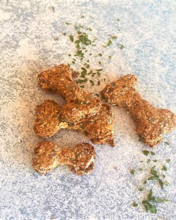 Bone-shaped dog treats on a blue-gray background with dried parsley sprinkled around