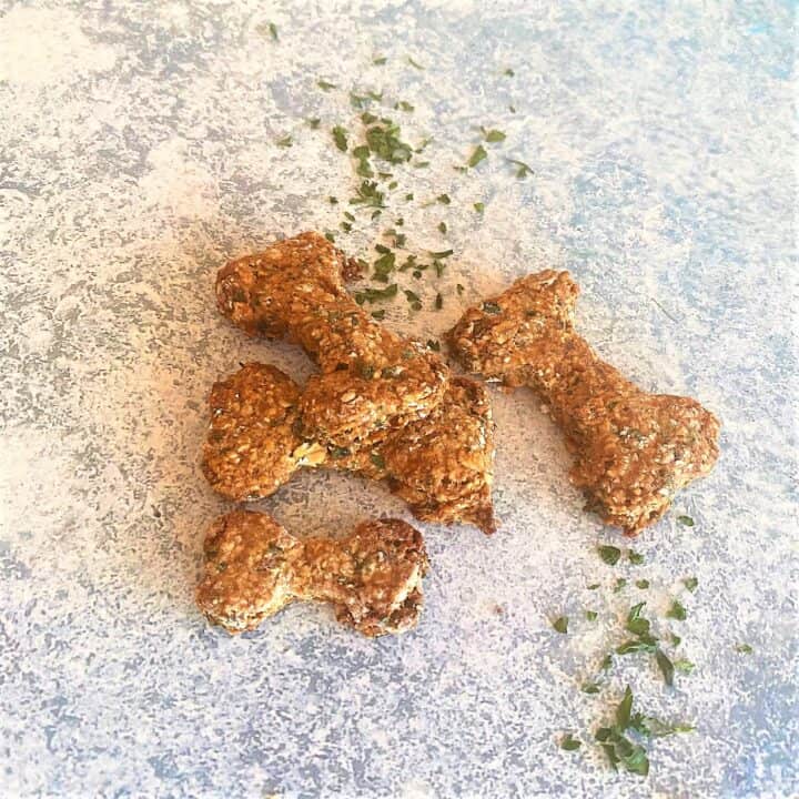 Bone-shaped dog treats on a blue-gray background with dried parsley sprinkled around