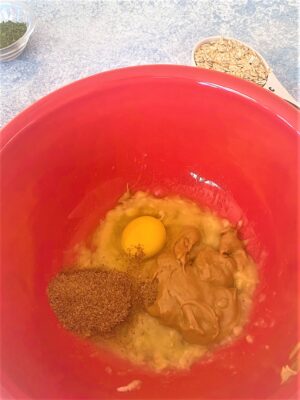 Red bowl with mashed banana, peanut butter, egg, and flax for dog treats i