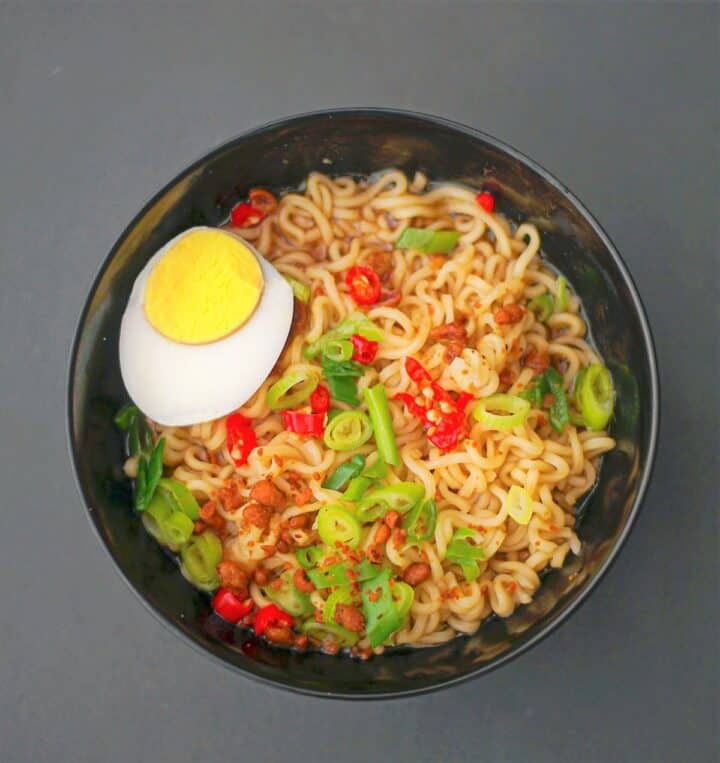 Bowl of ramen noodles with red chilies and half a boiled egg on gray background