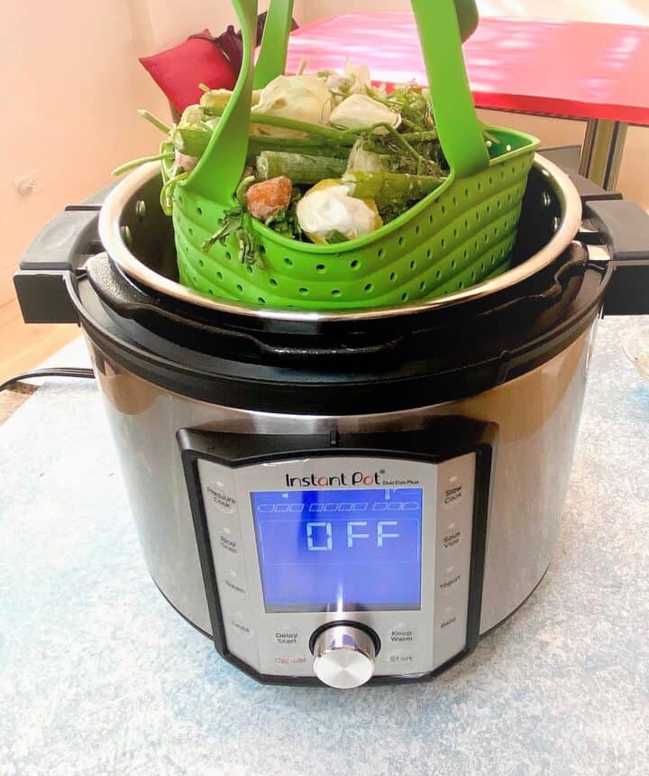 Putting green silicone steamer basket of frozen veggie scraps in the Instant Pot