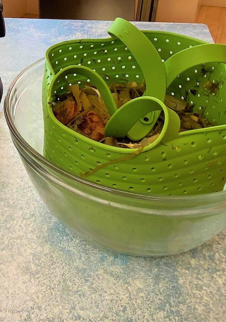 Green silicone steamer full of cooked veggie scraps cooling in a large, clear bowl