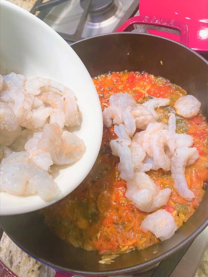 Adding raw, peeled shrimp to healthy jambalaya simmering in Dutch oven on gas cooktop