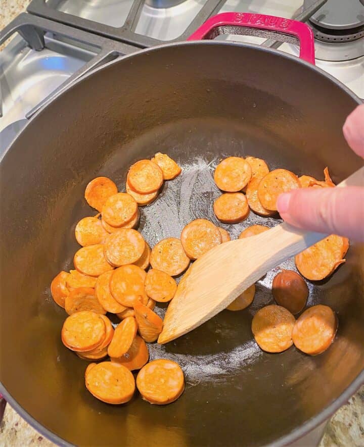 Chicken andouille sausage rounds being cooked in red Dutch oven on stovetop