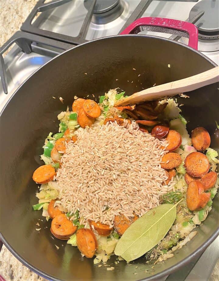 Adding rice, chicken andouille sausage rounds, and spices to vegetables in Dutch oven to make healthy jambalaya