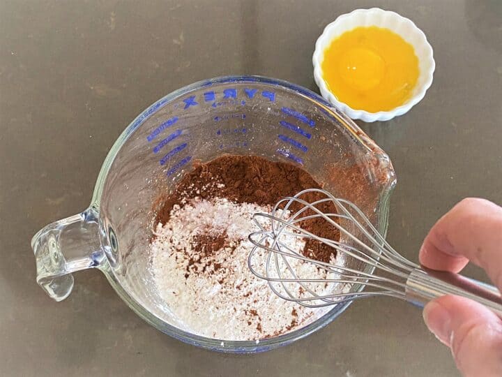 Whisking dry ingredients for no bake chocolate pie filling, with eggs yolks nearby ready to be added