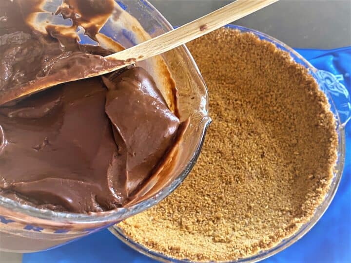 Pouring chocolate filling from large glass measuring cup into a [pie dish with graham cracker crust