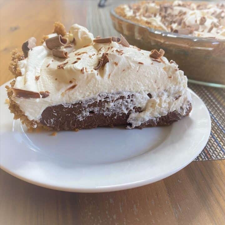 Cut wedge of No Bake Chocolate Pie viewed from the side with the pie in the background on wood grain surface