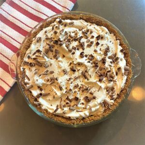 Whole No Bake Chocolate Pie with whipped cream and chocolate shavings and red-white striped cloth on brown background