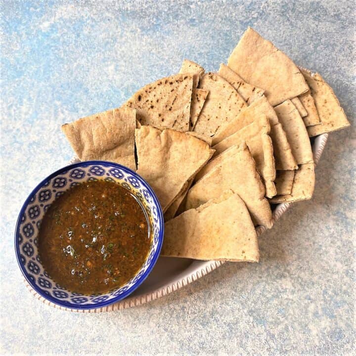 blue patterned bowl with red-brown dip and pita wedges in a white oval dish on a mottled bluish background