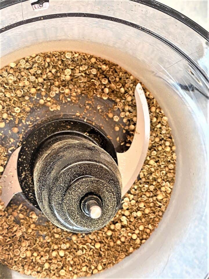 interior of food processor  containing halved brownish seeds and spice dust