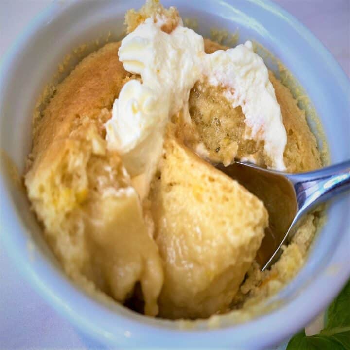 View of the interior of an orange pudding cake with saucy bottom and cake-like top with a bit of whip and a spoon