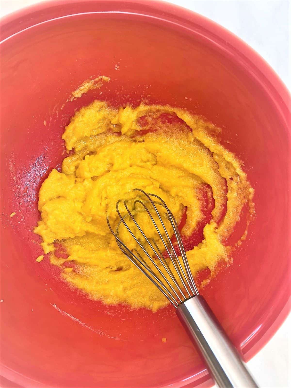 Bright yellow Egg yolk-sugar-butter mixture in red bowl with whisk