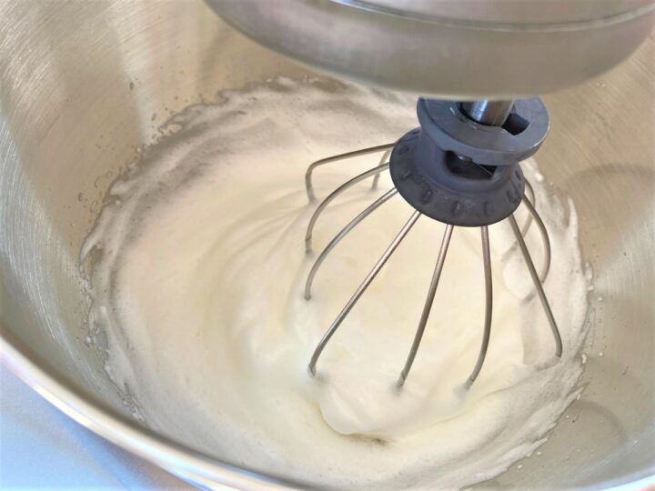 stiff beaten egg whites in the silver bowl of a stand mixer with a whisk attachment