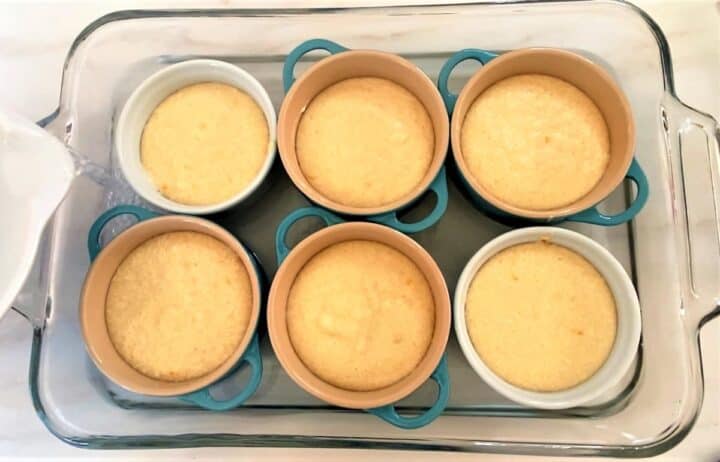 rectangular baking dish holding six ramekins with orange pudding cake batter inside and water surrounding them