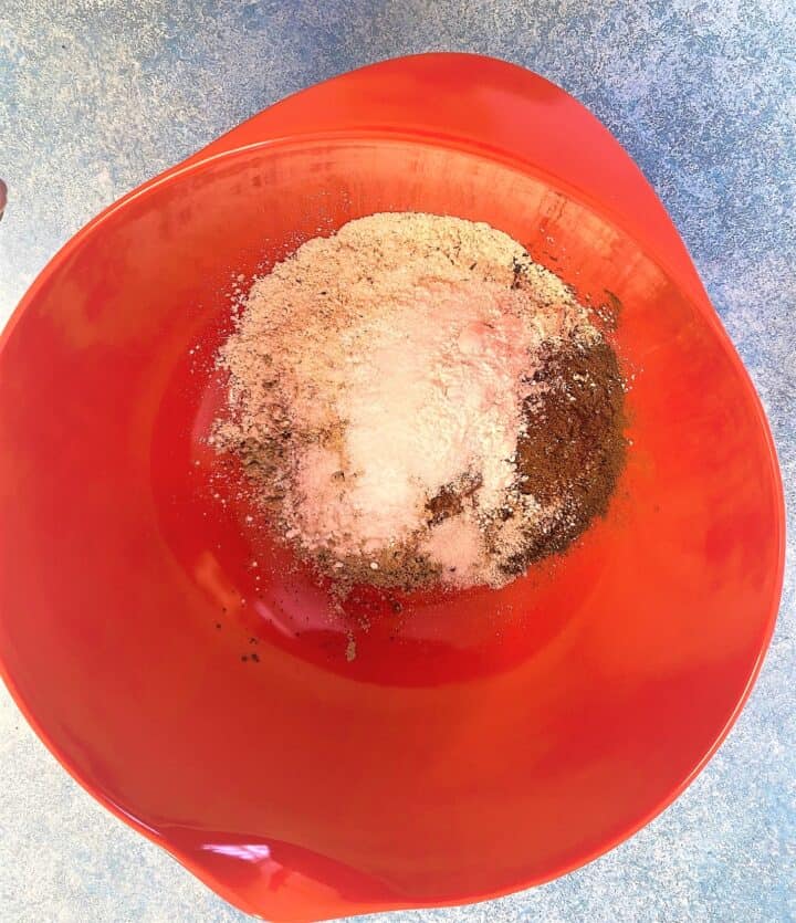 Red bowl with cocoa powder, flour and other dry ingredients sitting on a mottled blue countertop