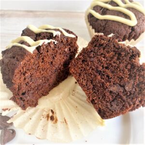 Chocolate muffin with white chocolate drizzle cut in half with muffin in background