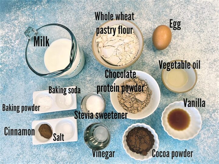 Ingredients for chocolate protein pancakes with labels on mottled blue countertop