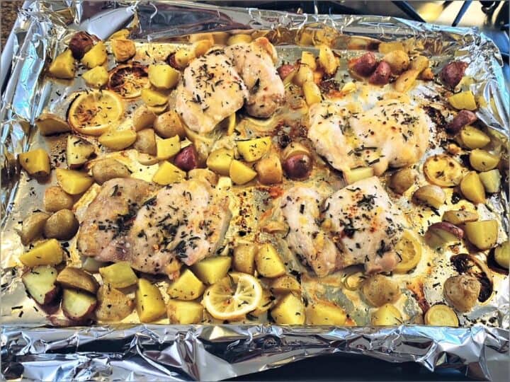 Cooked chicken thighs with potato chunks and lemon on a sheet pan