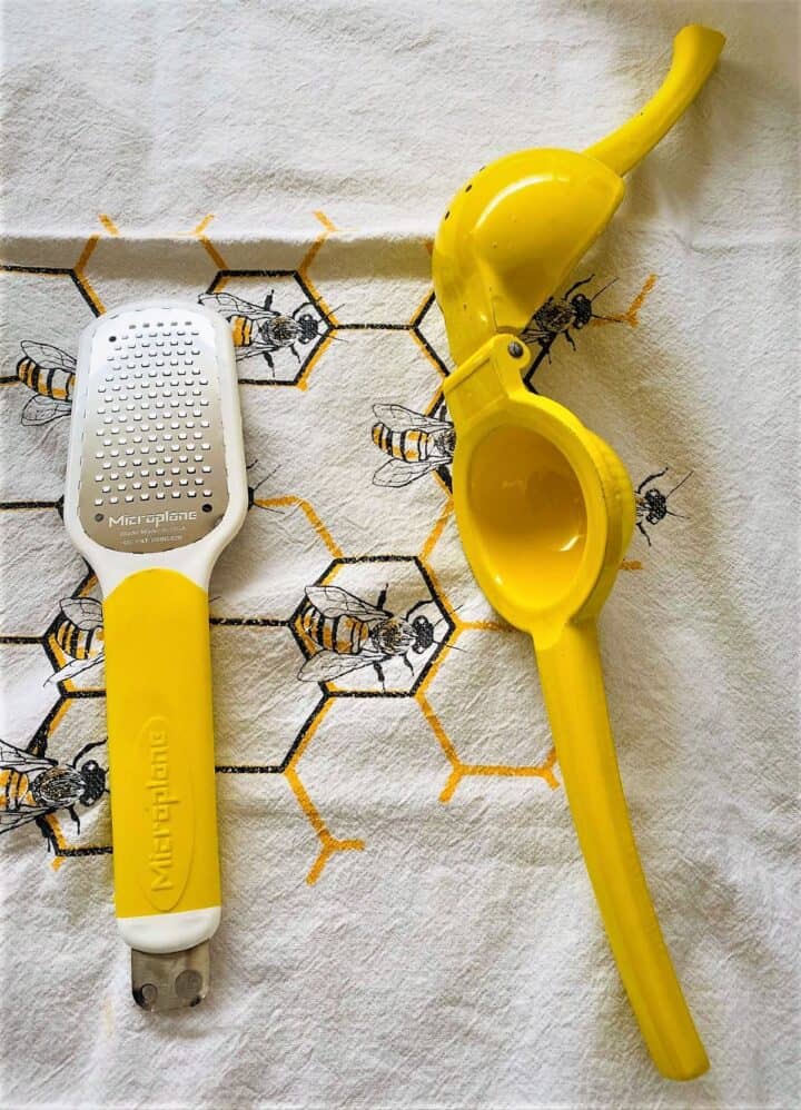 Grater with yellow handle and bright yellow lever citrus juicer on a bee pattern kitchen towel